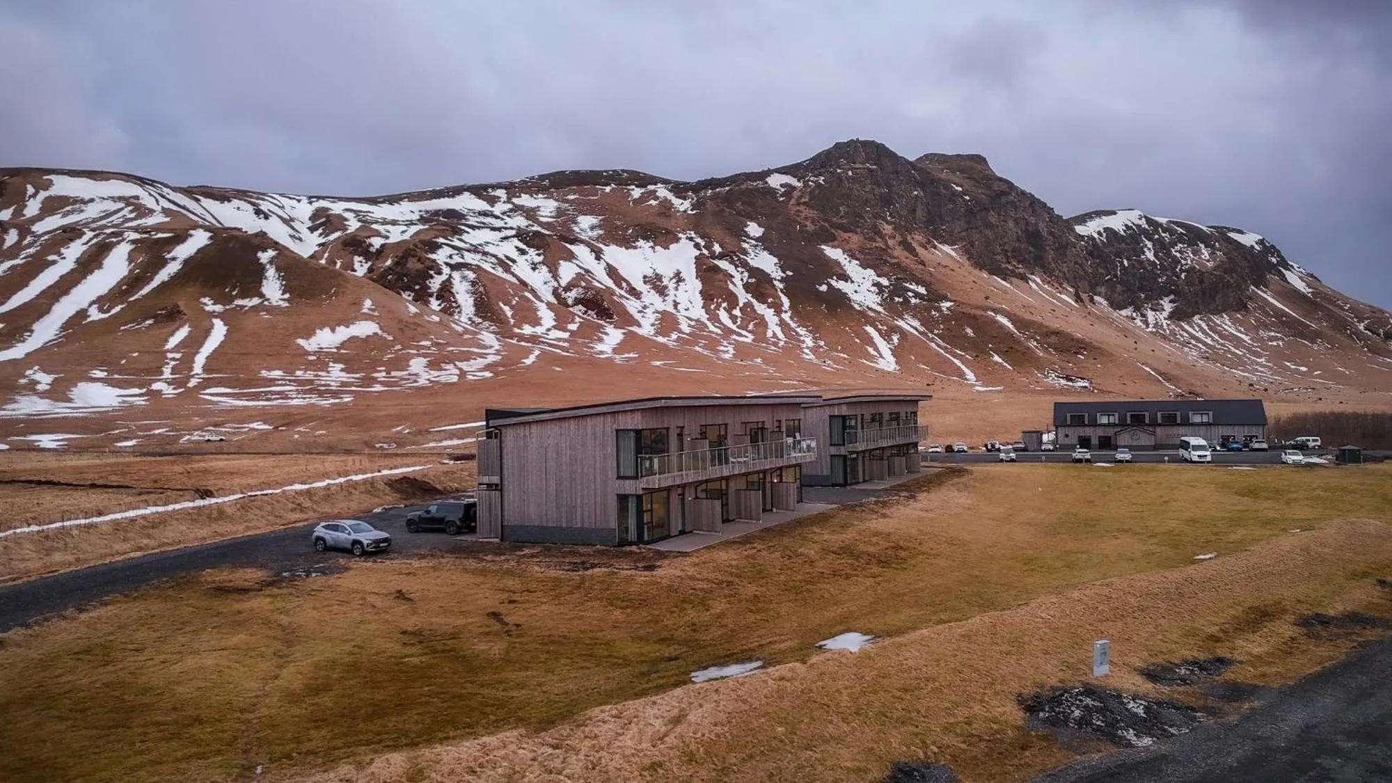Black Beach Suites — timber-clad studio apartments below a snow-streaked mountain near Vík, South Iceland