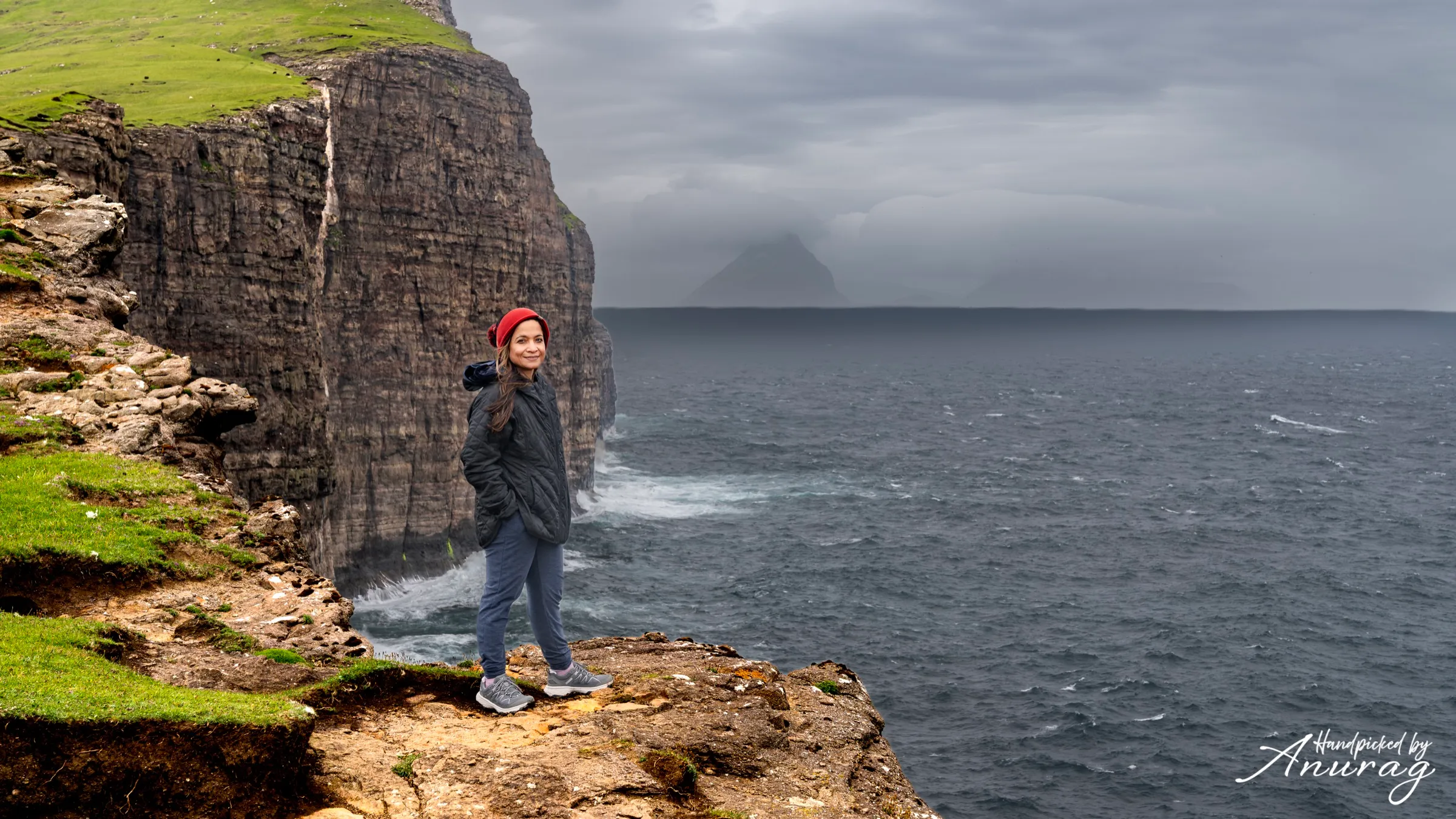 A hiker on a green clifftop ridge above the sea